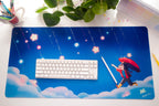 Blue desk mat with ADHD Alien character holding an umbrella. There are a keyboard, and stationery items on the desk.