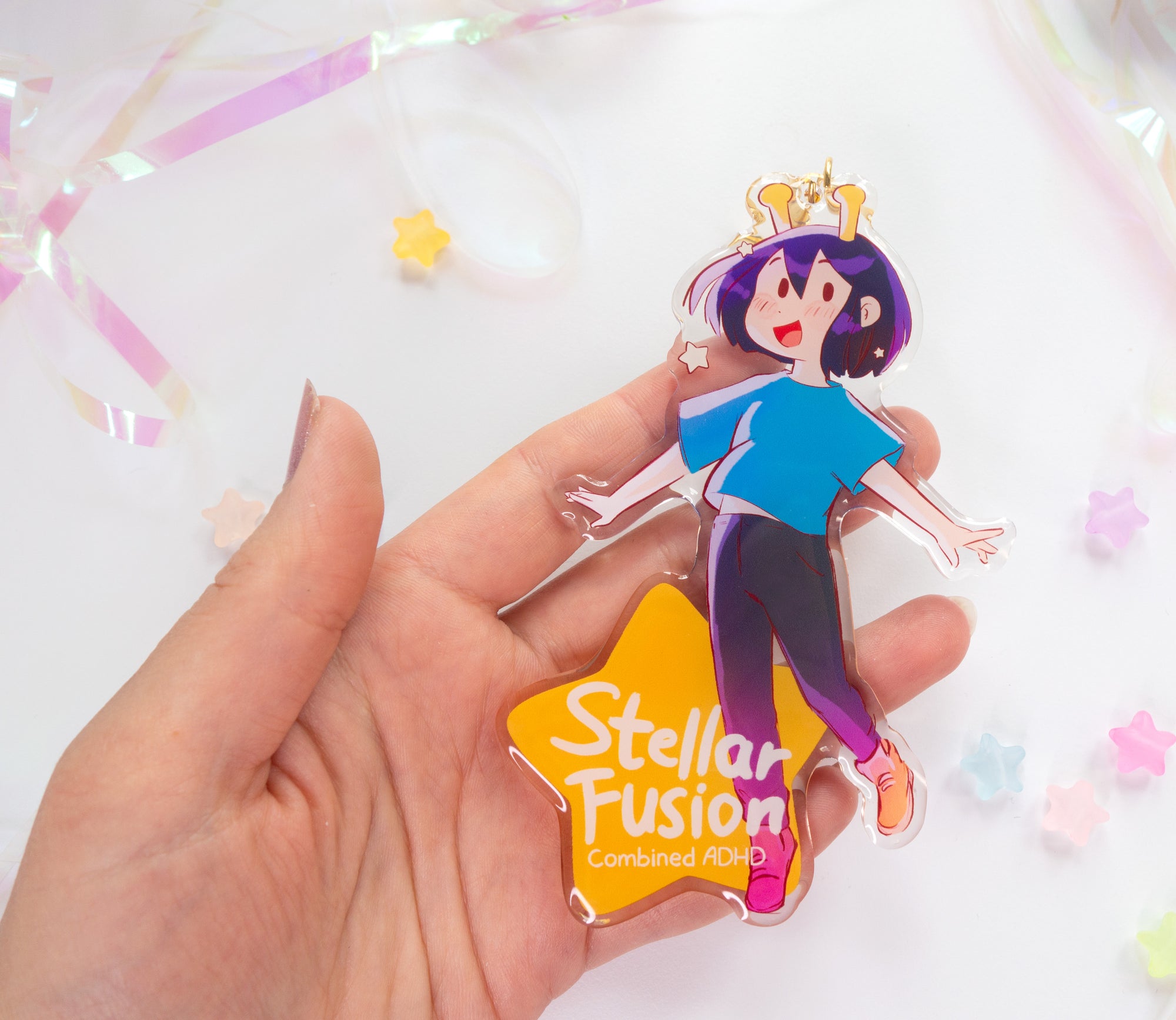 Hand holding the acrylic charm with 'Stellar Fusion' text on the star part over a white background
