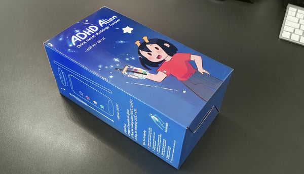 Blue box with a graphic of ADHD Alien holding the tumbler on a gray surface - Making of image 4