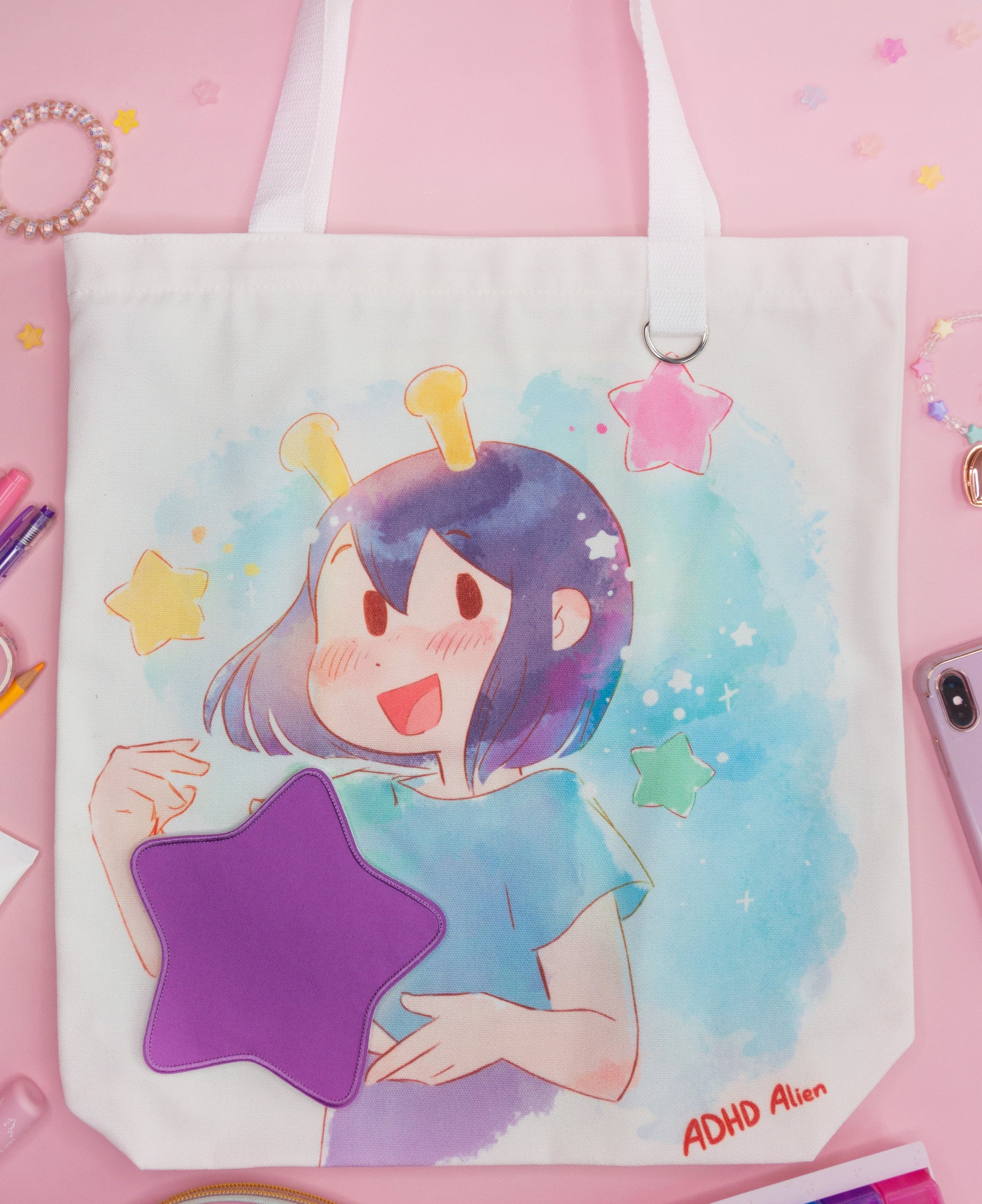 Tote bag with an illustration of the ADHD Alien character holding a star patch on a pink background