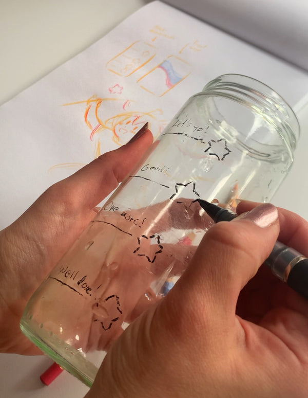 Hand holding a glass with a hand drawing the prototype design with a marker on it - Making of image 2
